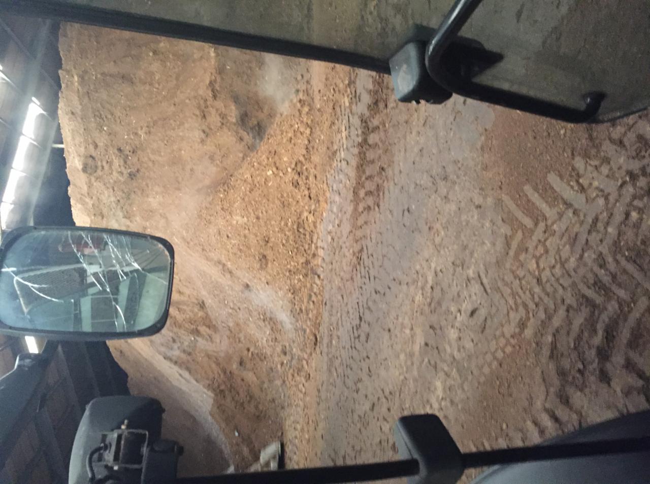 Widok z kabiny maszyny rolniczej na pryzmę brązowego materiału sypkiego, prawdopodobnie nawozu, z widocznymi śladami opon.