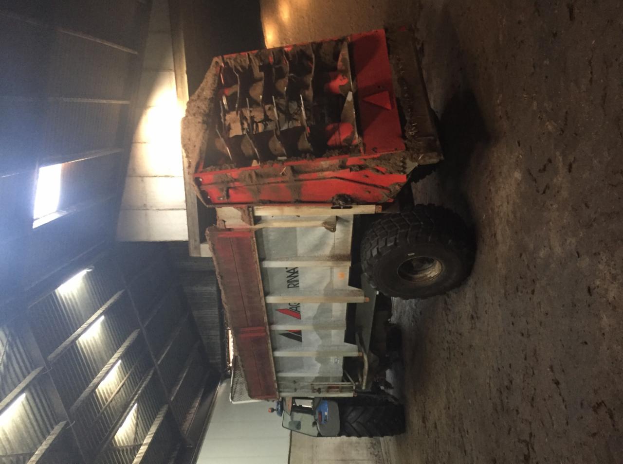 Rozrzutnik obornika marki Agrimaster Rima, częściowo wypełniony, stojący wewnątrz budynku gospodarczego z widocznym oknem dachowym.