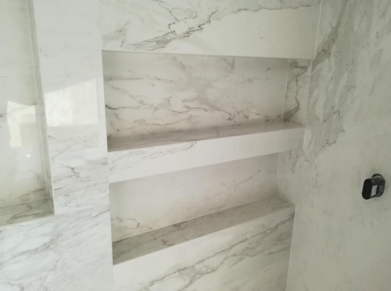 Wnęki ścienne wykończone białym marmurem z szarymi żyłami, tworzące półki w łazience.