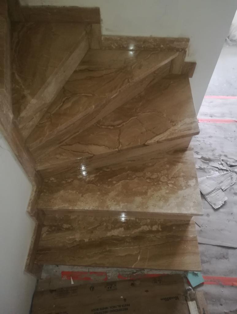 Kremowe, marmurkowe stopnie schodowe z widocznymi żyłami, prowadzące w górę, z fragmentem kartonu na podłodze.