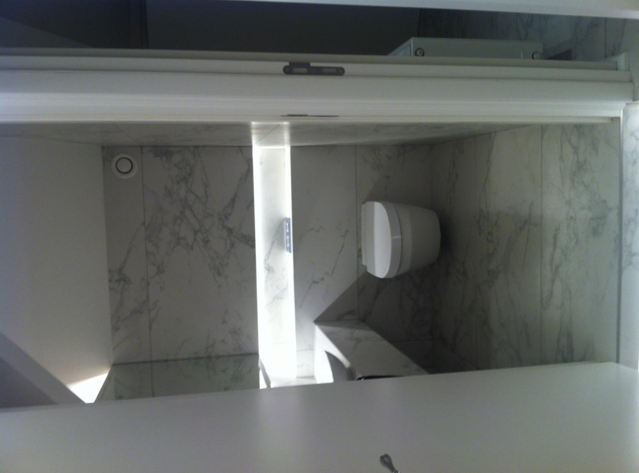 Nowoczesna toaleta podwieszana w łazience wykończonej płytkami imitującymi marmur, z oświetleniem LED w pionowej wnęce.