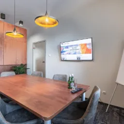 Sala konferencyjna w Białymstoku z dużym drewnianym stołem, szarymi krzesłami, telewizorem wyświetlającym stronę internetową z napisem 'Biuro Rachunkowe' oraz tablicą suchościeralną.