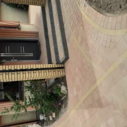 Ułożona kostka brukowa w odcieniach różu i beżu tworząca ścieżkę i schody przed wejściem do domu z ciemnymi drzwiami.