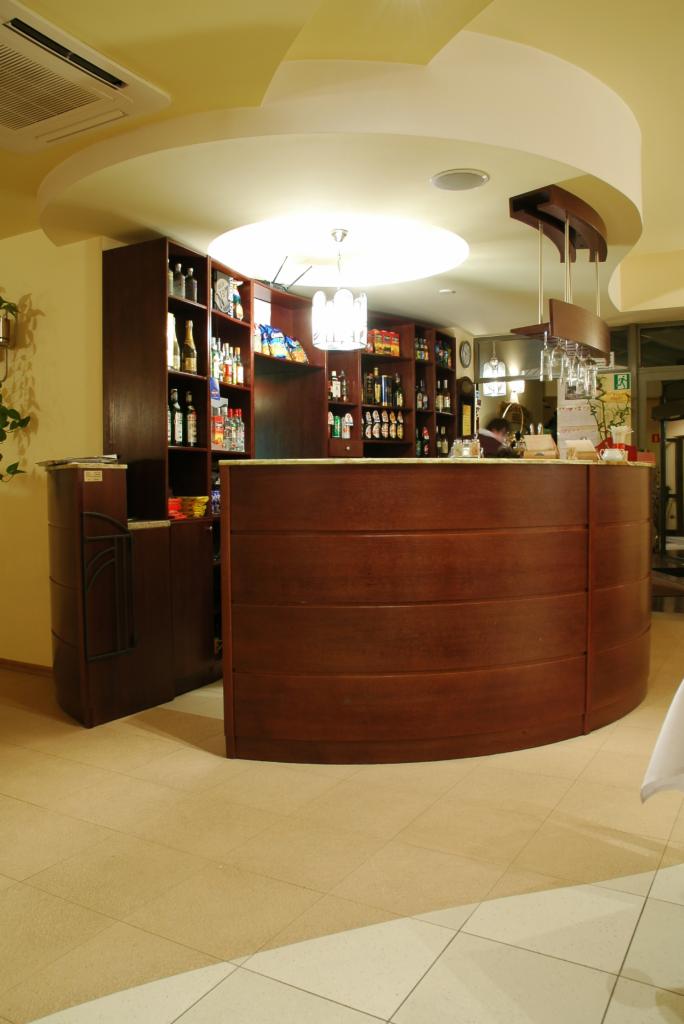 Bar w restauracji z drewnianą ladą i półkami z alkoholem, oświetlony lampą wiszącą i światłem z sufitu.