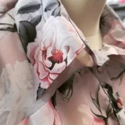 Detale koszuli damskiej z delikatnego materiału w kwiatowy wzór, widoczny kołnierzyk i staranne szwy.