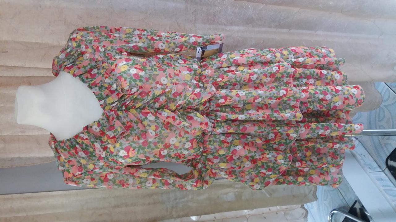 Sukienka mini z falbanami w drobny kwiatowy wzór, prezentowana na manekinie bez głowy, częściowo widoczny metalowy wieszak, tło stanowi beżowa tkanina.