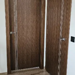 Dwa skrzydła drzwiowe w kolorze ciemnego drewna z trzema srebrnymi paskami, zamontowane w jasnym wnętrzu z drewnianą podłogą.