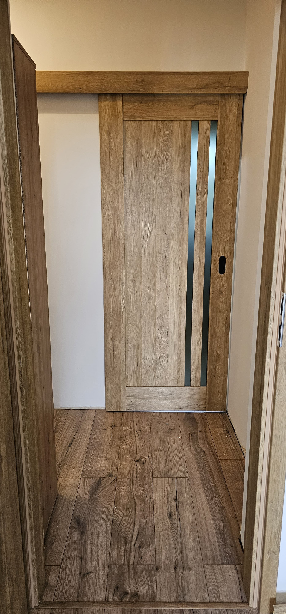 Zamknięte przesuwne drzwi wewnętrzne z drewnianą okleiną i trzema pionowymi przeszkleniami, widoczne z perspektywy podłogi z paneli imitujących drewno.