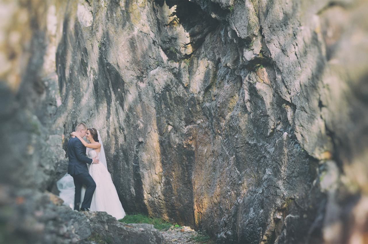 Para młoda w objęciach na tle skalnej ściany z nieregularną fakturą i zielonymi akcentami mchu u podstawy.
