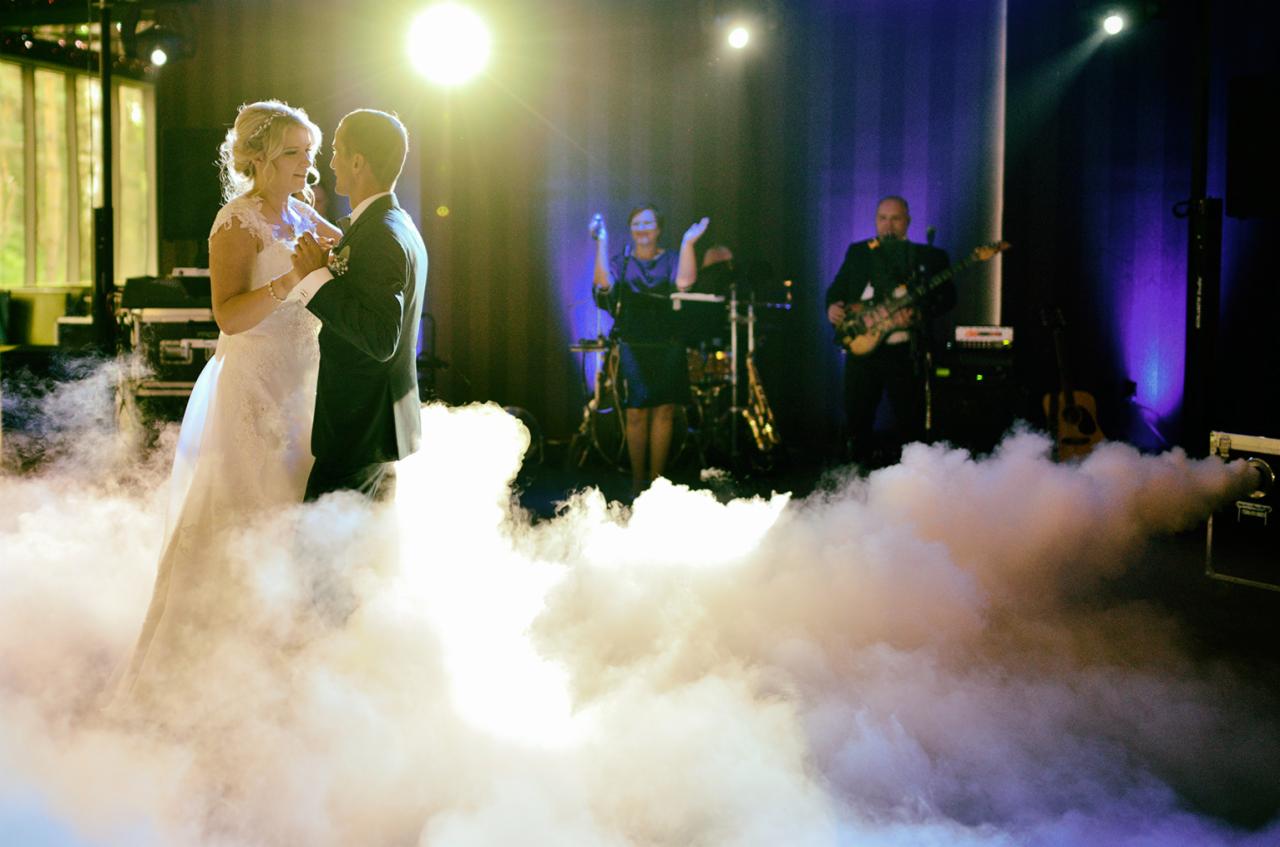 Para młoda tańczy pierwszy taniec w chmurach dymu na tle zespołu muzycznego podczas wesela.
