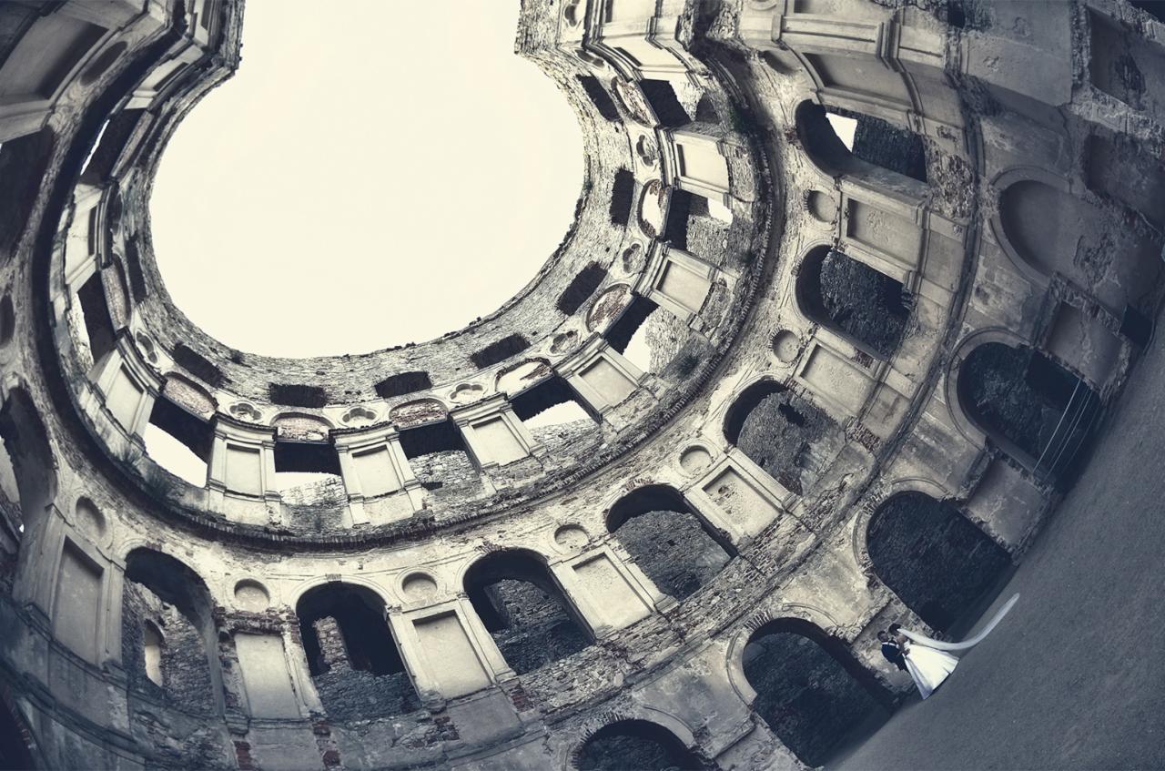Para młoda w ruinach zamku sfotografowana z perspektywy żabiej, widok na niebo przez okrągły otwór w dachu.