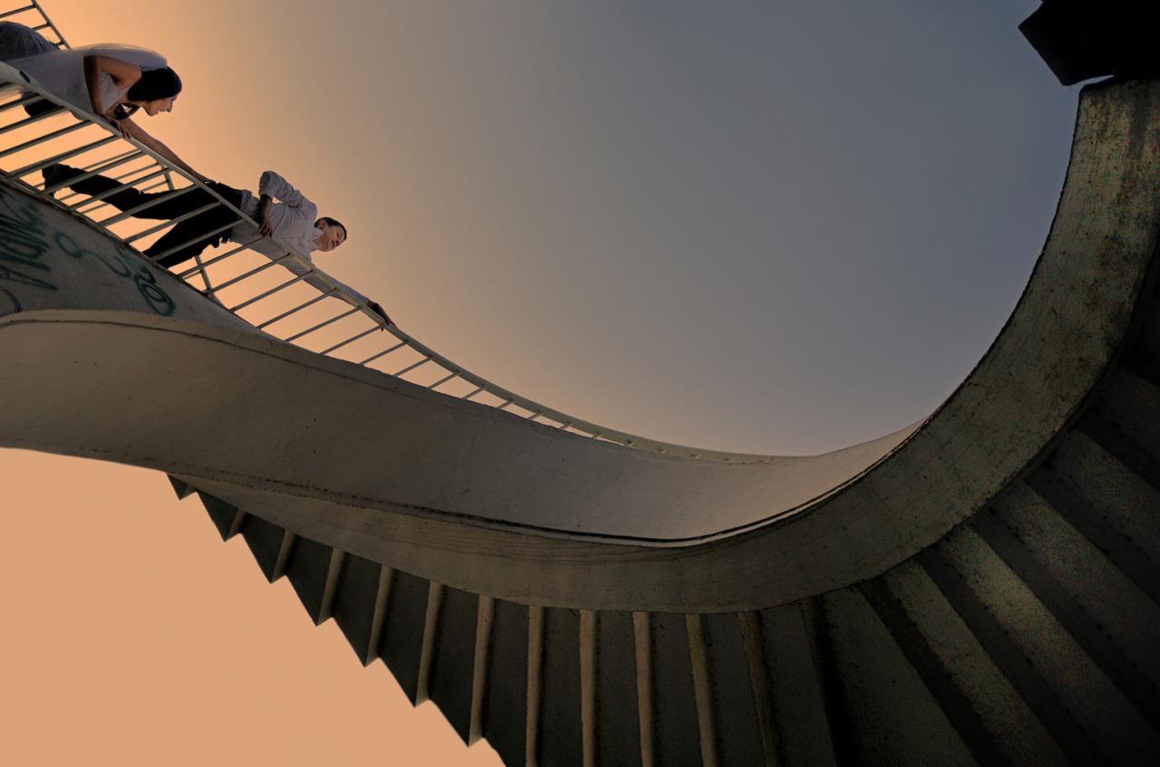 Para w trakcie sesji narzeczeńskiej na spiralnych schodach z graffiti, ujęcie z dołu, ciepłe oświetlenie.