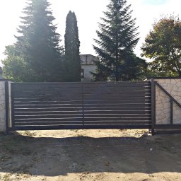 Kuźnia Macieja - Nowoczesna przesuwna brama wjazdowa z poziomych profili, z delikatnym logo firmy w rogu, zamontowana na kamiennym murku, widok z zewnątrz na tle drzew i zabudowań.