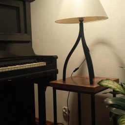Kuźnia Macieja - Lampa stojąca z abażurem na metalowym stoliku w stylu loft, obok czarnego pianina i rośliny doniczkowej, oświetlona ciepłym światłem.