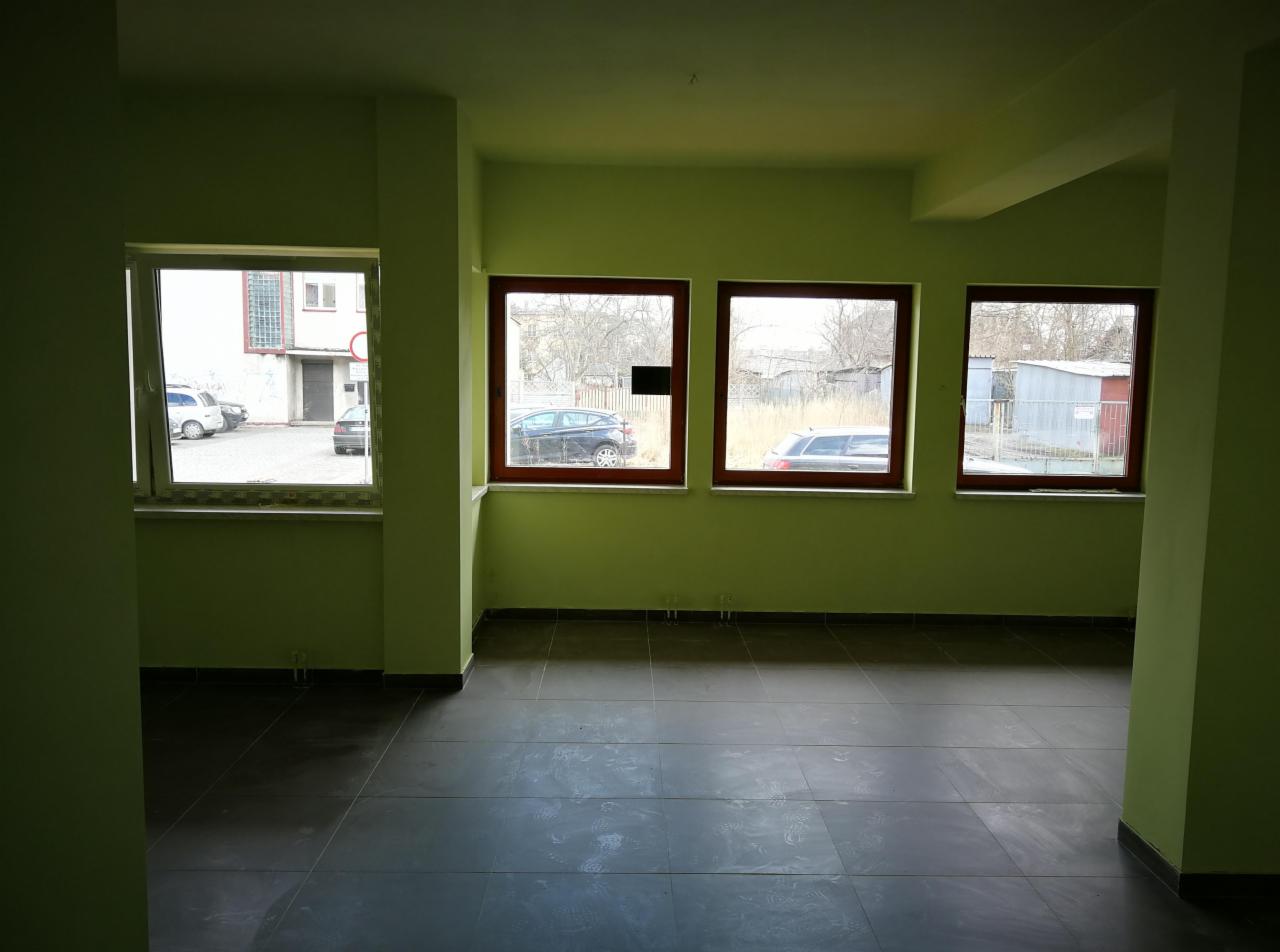 Puste, zielone biuro z szarą podłogą z płytek, widok na parking przez okna w drewnianych ramach.