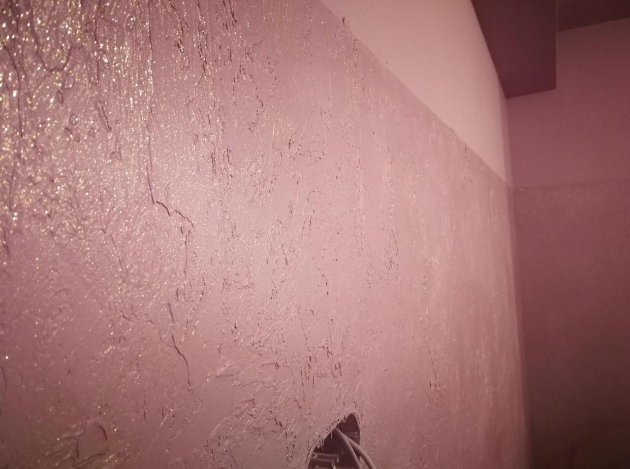 Ściana pokryta dekoracyjną, różową strukturą z widocznym otworem na instalację elektryczną i fragmentem sufitu w tle.