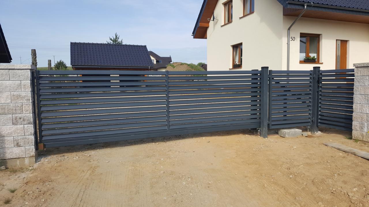 Nowoczesna, przesuwna brama wjazdowa z poziomych profili w kolorze grafitowym, zamontowana na posesji z domem jednorodzinnym o jasnej elewacji i numerze 50, widoczna z zewnątrz.