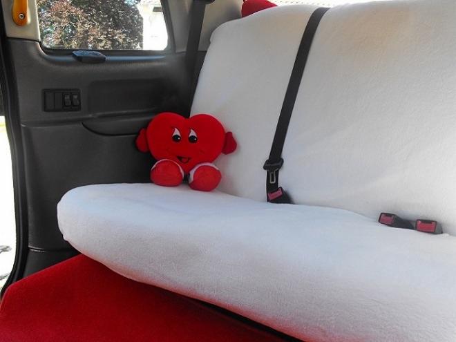 Wnętrze samochodu z białymi pokrowcami na siedzeniach i pluszowym sercem opartym o zagłówek