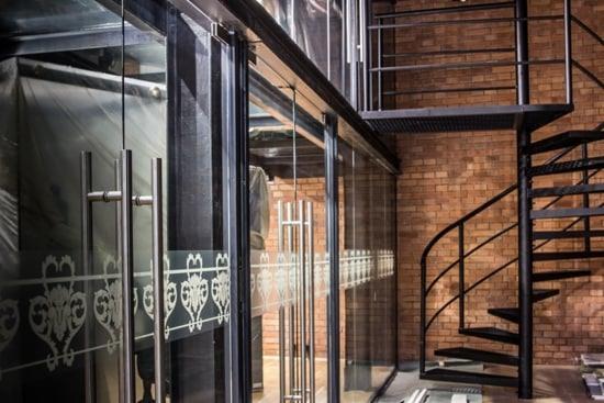Szklane drzwi z ozdobnym wzorem w biurze z ceglaną ścianą i spiralnymi schodami.