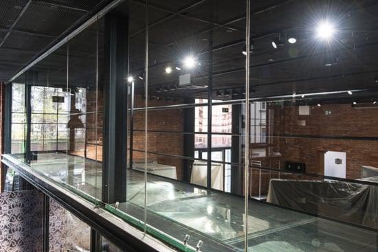 Szklana podłoga i balustrada w loftowym wnętrzu z ceglaną ścianą, widok z góry na konstrukcję z metalowymi ramami i przezroczystym szkłem.