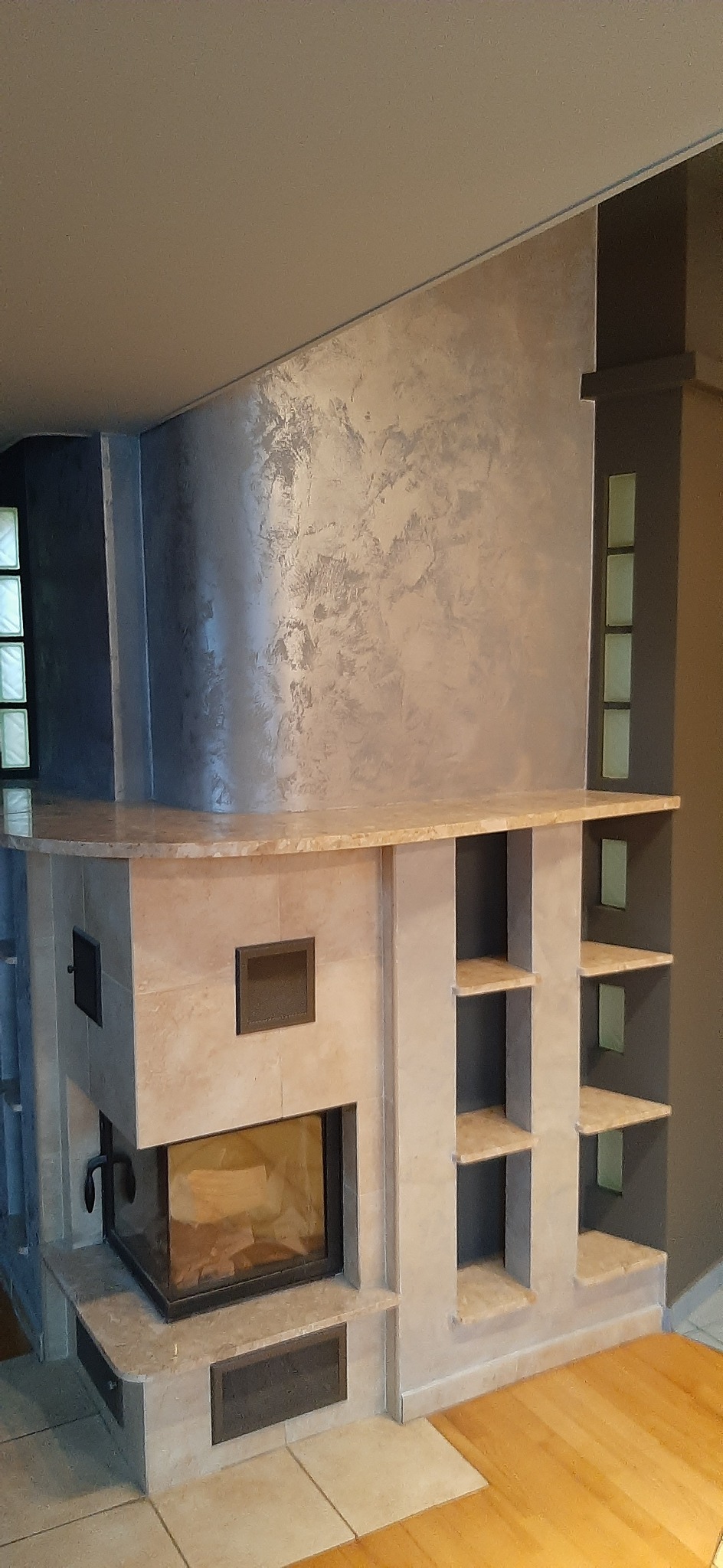 Wykończony kominek z obudową z płytek imitujących kamień, z półkami i dekoracyjną ścianą w odcieniach szarości.