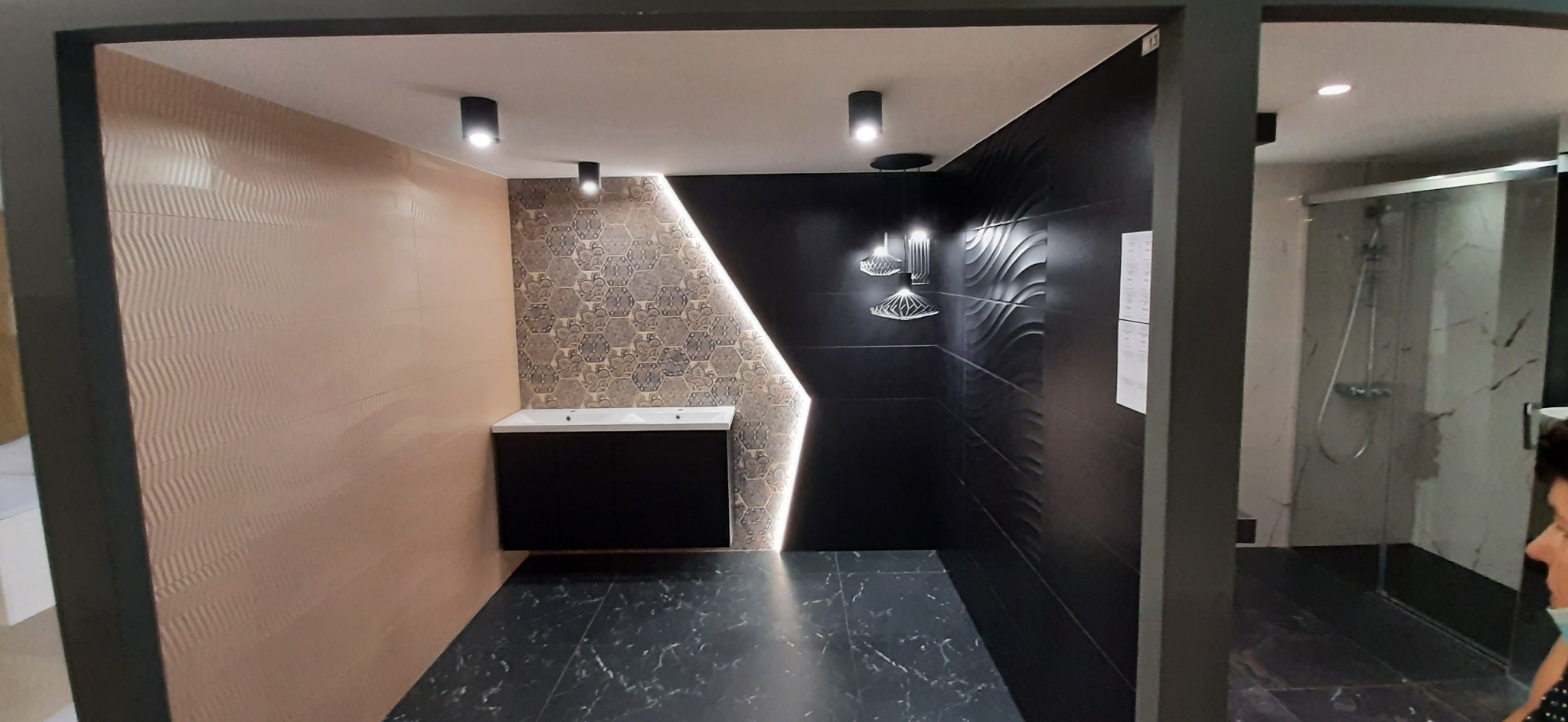 Nowoczesna aranżacja łazienki z płytkami w odcieniach beżu, czerni i szarości, marmurowa podłoga, umywalka z szafką, oświetlenie punktowe i dekoracyjne lampy wiszące.