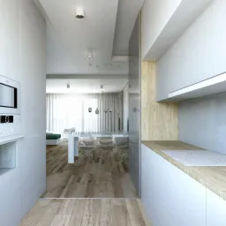 Wnętrze jasnej kuchni otwartej na salon z parkietem, białymi meblami, przezroczystymi krzesłami i wiszącymi lampami.