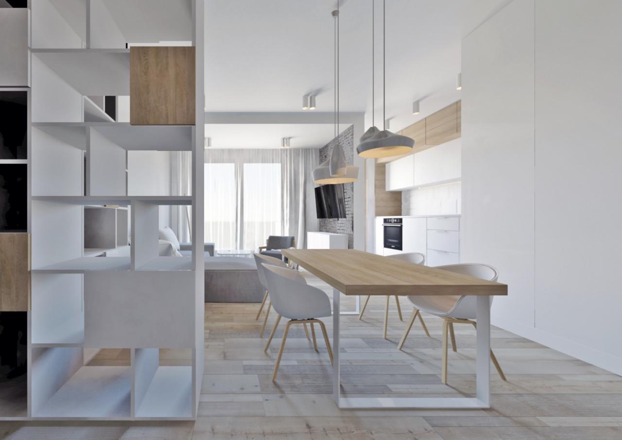 Jasne, przestronne wnętrze mieszkania we Wrocławiu z drewnianym stołem, białymi krzesłami i regałem z półkami w odcieniach bieli, szarości i drewna, widok na salon z szarą sofą i kuchnię z białymi...
