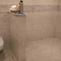 Wykończona łazienka w jasnych płytkach z toaletą podwieszaną, fragmentem wanny i akcesoriami na p&oacute;łce; widoczne wzory na podłodze.