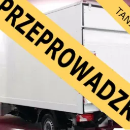 Biały samochód dostawczy z napisem 'PRZEPROWADZKI TANIO' na żółtym banerze, widok z boku na tle drzew.