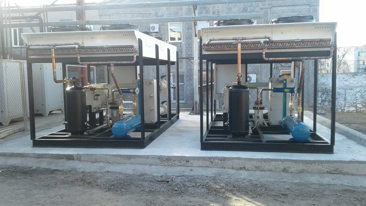 Dwie przemysłowe jednostki chłodnicze na zewnątrz budynku, każda z czarną ramą, białym panelem górnym i widocznymi rurami miedzianymi, umieszczone na betonowej platformie.