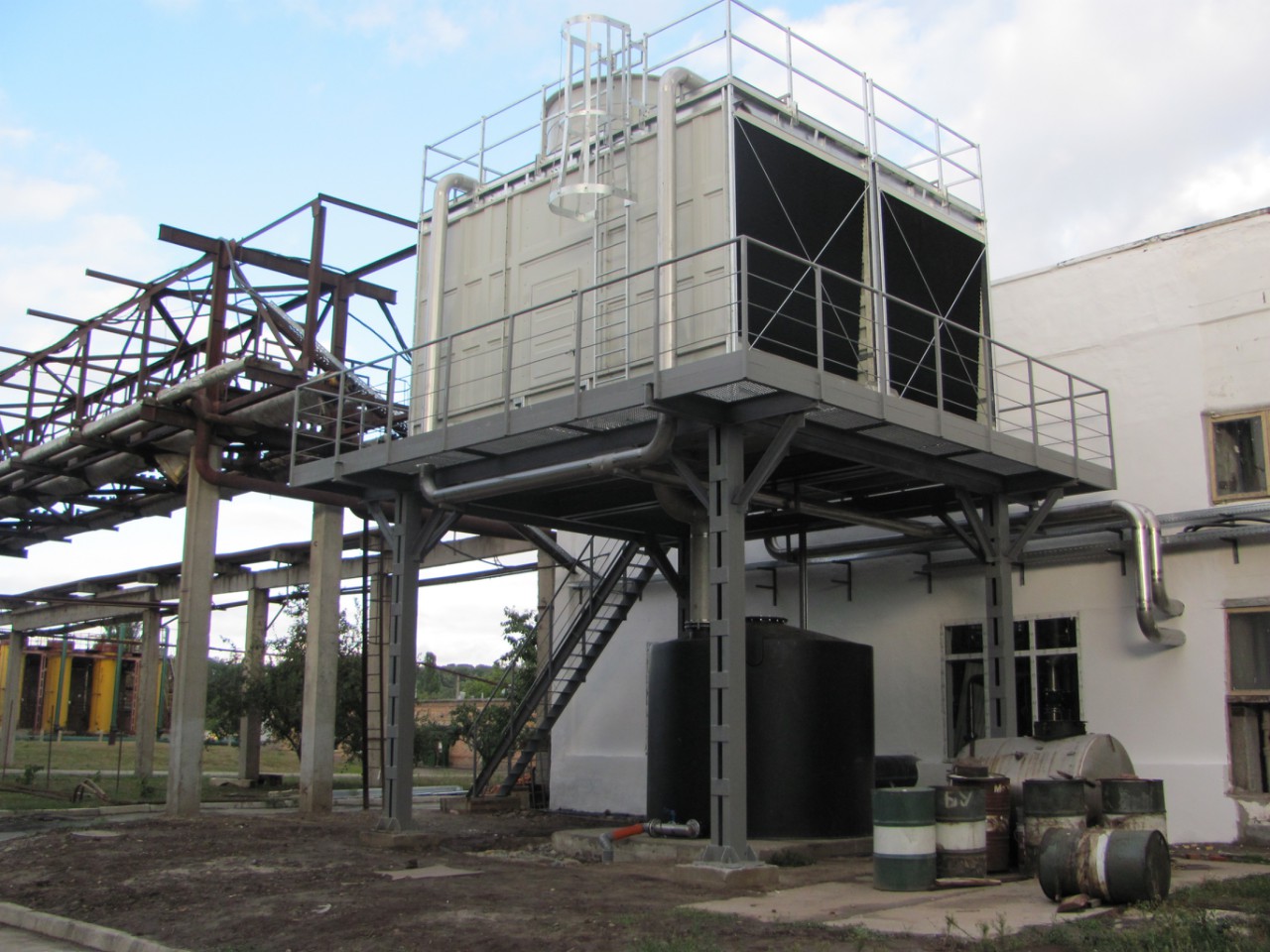 Zewnętrzna instalacja chłodnicza na stalowej platformie z balustradami, rurociągi i zbiorniki w tle, widoczne także elementy konstrukcji stalowej.