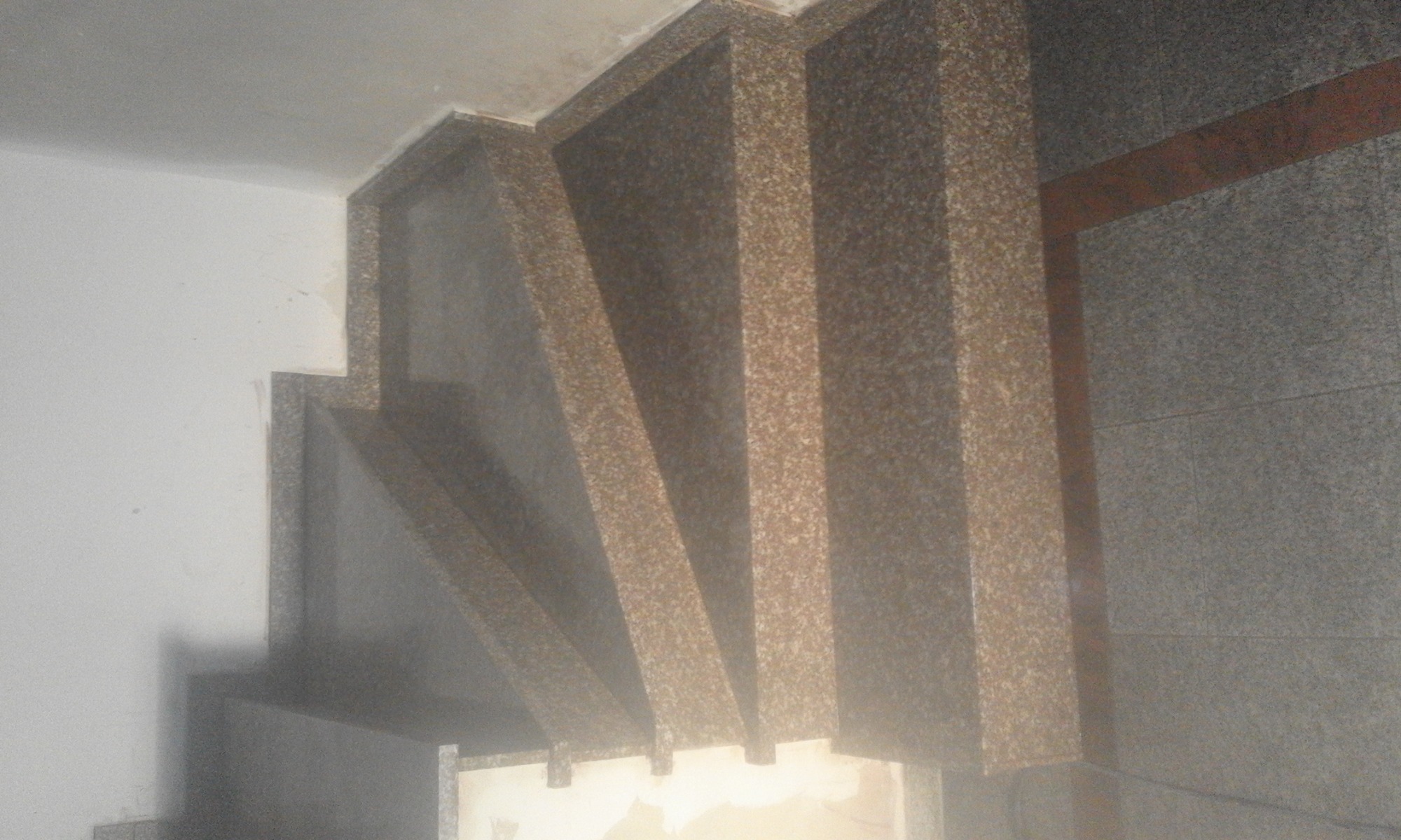 Wykończenie wnęki schodowej płytami imitującymi piaskowiec, widoczne fragmenty białej ściany i szarej okładziny ściennej.