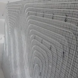 Białe rurki systemu rozprowadzania ciepła ułożone na podłodze pokrytej matą z rastrem w kwadraty, przygotowane do zalania wylewką.