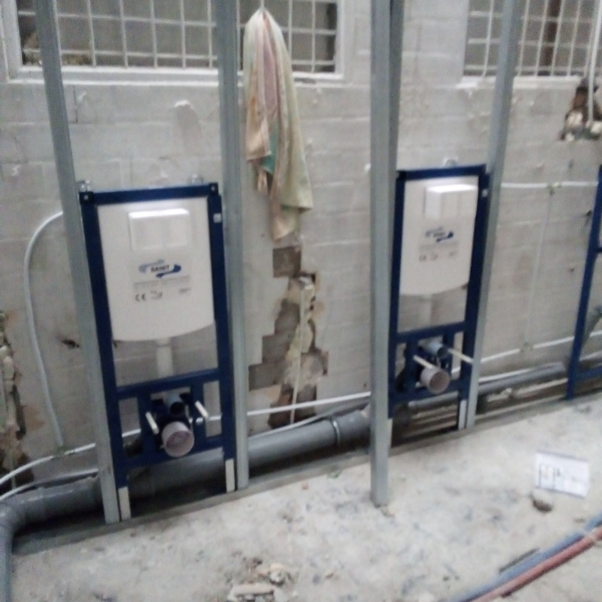 Stelaż podtynkowy WC zamontowany w łazience w trakcie remontu, widoczne rury kanalizacyjne i fragment ściany z ubytkiem tynku.