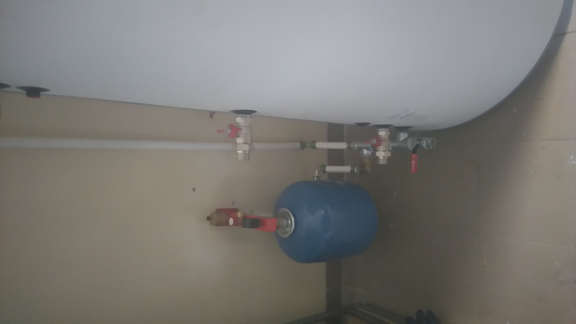 Zamontowany, niebieski zbiornik przeponowy z czerwonym zaworem bezpieczeństwa pod bojlerem, widoczne rury i zawory doprowadzające wodę.
