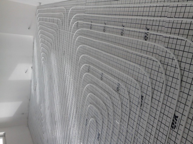 Białe rurki systemu rozprowadzania ciepła ułożone na podłodze pokrytej matą z rastrem w kwadraty, przygotowane do zalania wylewką.