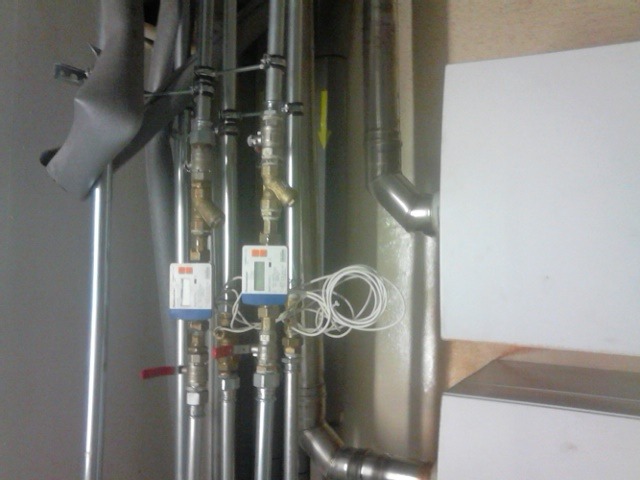 Rury instalacyjne z zaworami i licznikami, widoczne także fragmenty kotła grzewczego i izolacji rur.