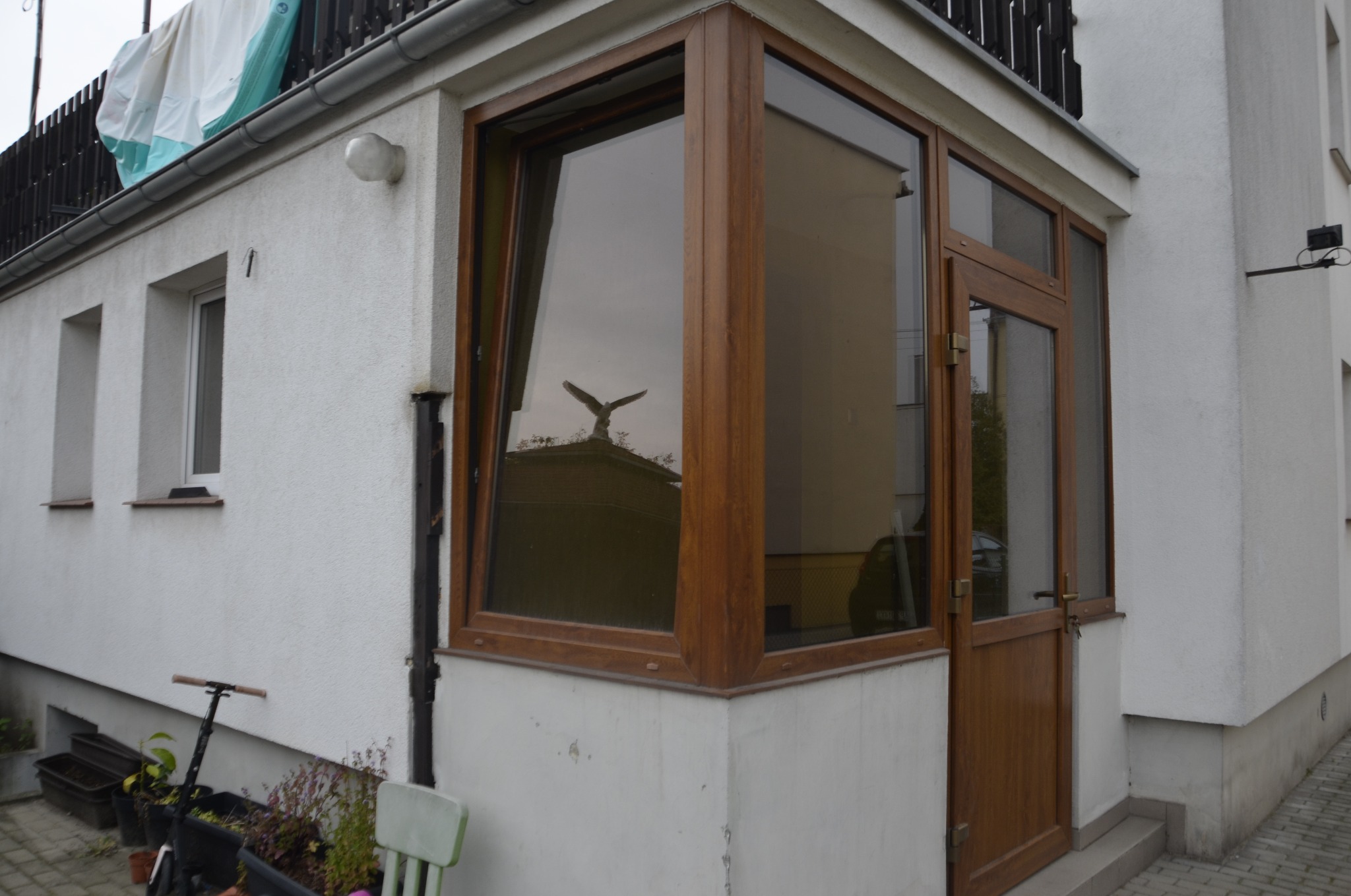Narożne okno i drzwi drewniane z widocznym odbiciem pomnika orła na tle białej elewacji budynku.