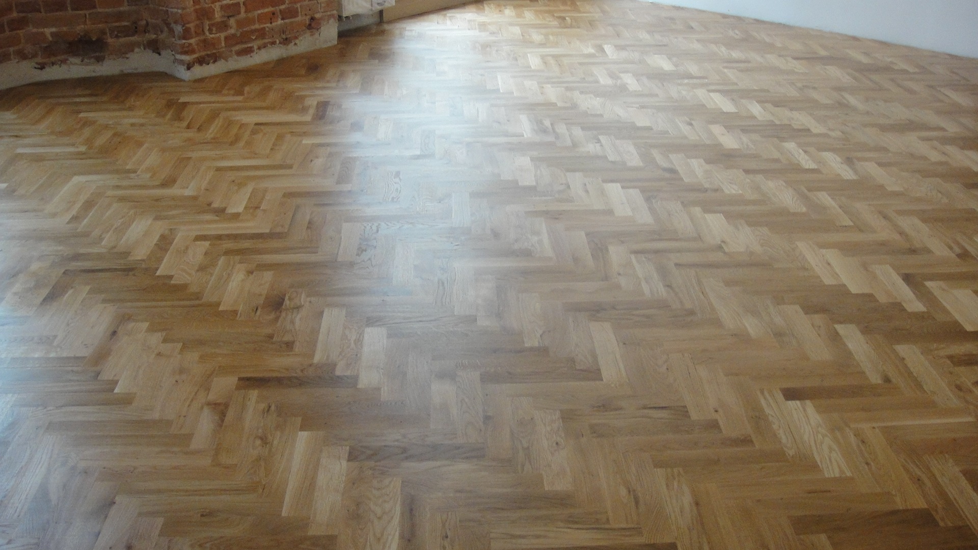 Ułożony w jodełkę, lakierowany parkiet dębowy w Zgierzu, z widocznym fragmentem ceglanej ściany w tle.