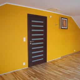 Firma Expert - Pokój na poddaszu po odświeżeniu: ściany pomalowane na intensywny żółty kolor, brązowe drzwi z poziomymi przeszkleniami, parkiet na podłodze, obraz na ścianie.
