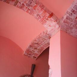 Firma Expert - Różowe wnętrze z ceglanymi łukami i dekoracyjną metalową ozdobą w kształcie stożka, ukazujące połączenie starej architektury i nowoczesnego designu.