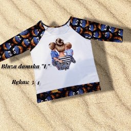 Anna Szulc - Damska bluza rozmiar L z rękawem 3/4, biały przód z nadrukiem kobiety obejmującej dwóch chłopców, rękawy i dół z wzorem ciasteczkowych potworów na czarnym tle, leżąca na piasku.