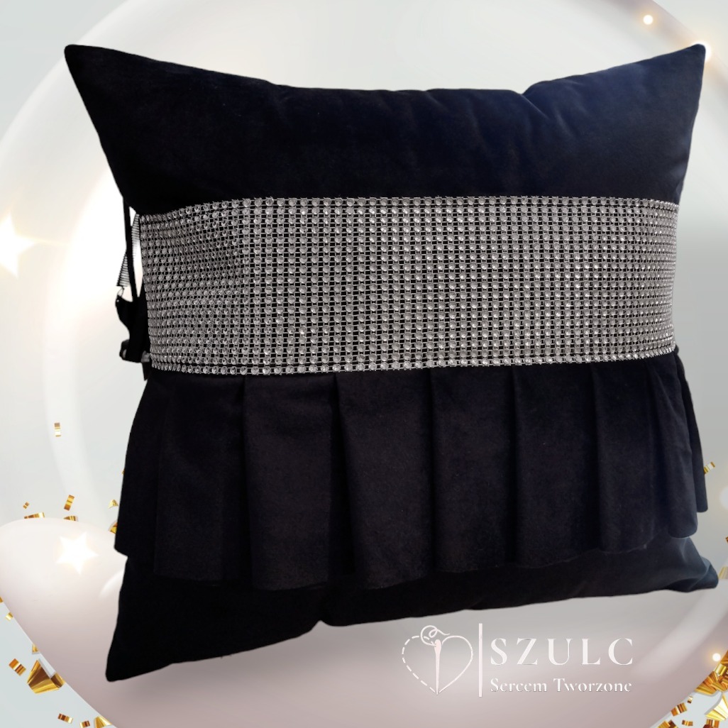 Czarna, aksamitna poduszka dekoracyjna z plisowaną falbaną i pasem z imitacji cyrkonii na białym, rozmytym tle z konfetti.