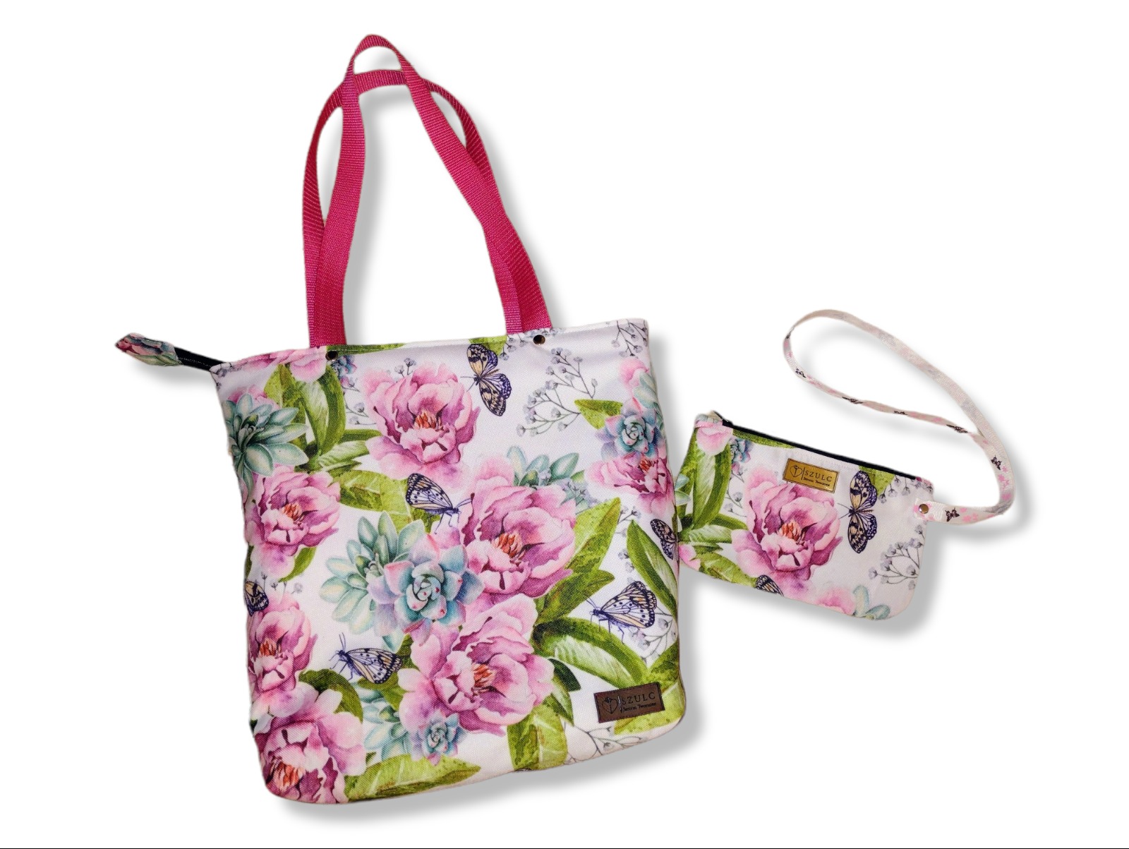 Biała torba na zakupy z różowymi uchwytami i pasująca mała kosmetyczka, obie w kwiatowy wzór z motywem motyli, leżące na białym tle.