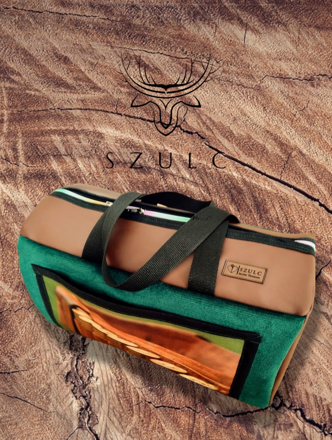 Torba podróżna z brązowej skóry ekologicznej i zielonego weluru z nadrukiem, wyprodukowana w Kluczborku, leży na tle imitującym strukturę drewna. Widoczne logo producenta.