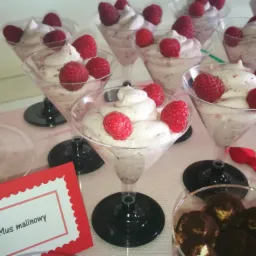 Deser mus malinowy w kieliszkach martini, udekorowany świeżymi malinami, obok deser tiramisu i wizytówka z nazwą deseru.