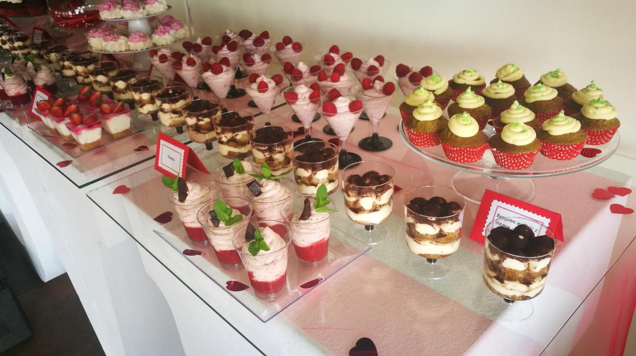 Szwedzki stół z różnorodnymi deserami w szklanych naczyniach: mini serniki z truskawkami, tiramisu, mus malinowy z dekoracją z malin, babeczki z zielonym kremem na paterze, dekoracja stołu...