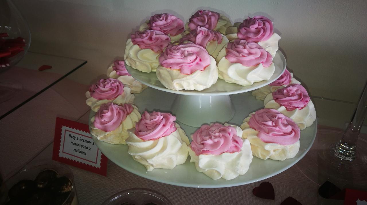 Dwupoziomowa patera z bezami udekorowanymi kremem mascarpone z malinami w kształcie róż, widoczna etykieta z nazwą deseru i dekoracje w kształcie serc.