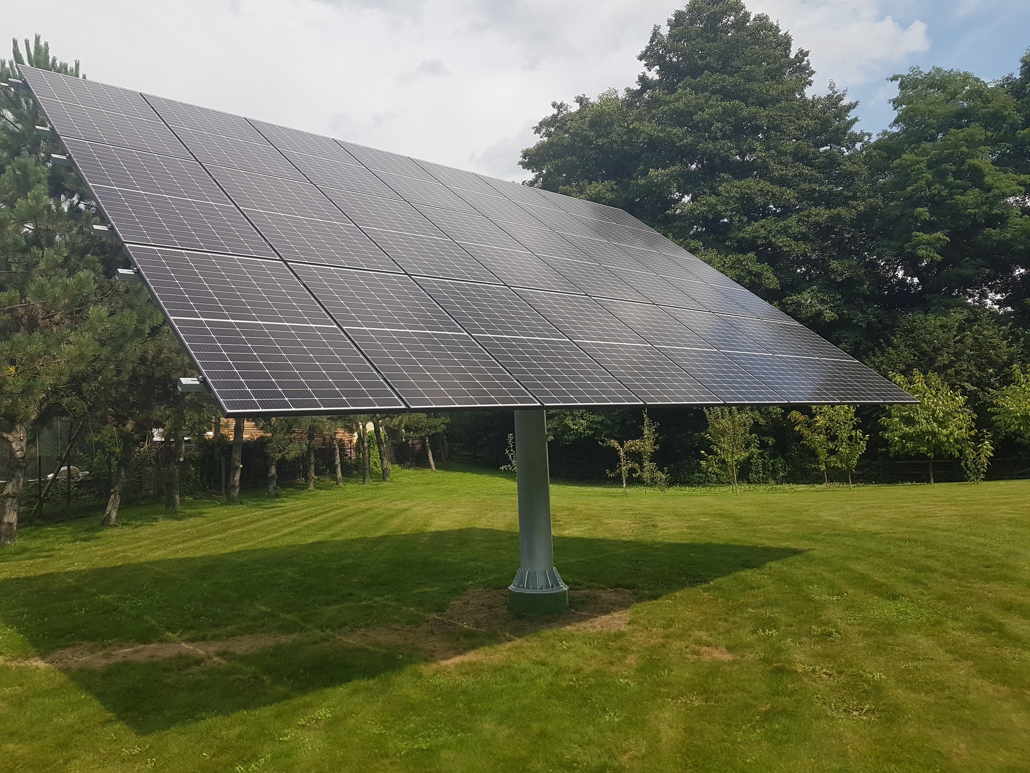 Panel słoneczny z trackerem w Miękini, podążający za słońcem na tle zielonego trawnika i drzew.